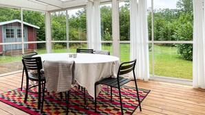 Ein Wintergarten mit rundem Tisch und Stühlen, einem bunten Teppich und Blick auf einen grünen Garten.