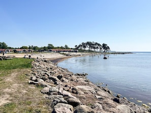A coastal area with a rocky shoreline, a clear sky, and a row of houses in the background. - 5 Person Holiday Home in Farjestaden (Farjestaden)