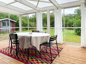 A conservatory with a round table and chairs, a colorful rug, and a view of a green landscape. - 5 Person Holiday Home in Farjestaden (Farjestaden)
