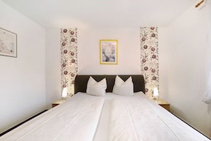 Een net opgemaakt bed met witte lakens, een donkere hoofdbord en twee bedlampjes.