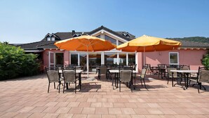 A patio with outdoor seating and umbrellas, a building with a tiled roof, and a clear sky.