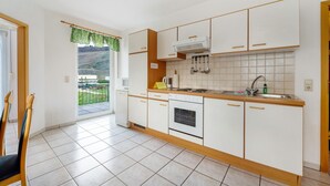 A kitchen with white cabinets, a stove, a sink, and a window with a view of a green landscape.