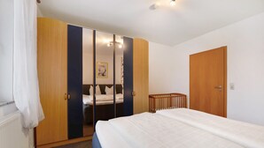 A bedroom with a bed, a wardrobe, a crib, and a mirror.