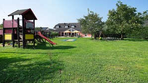 A playground with a slide and climbing structures, a trampoline, and a building with a sloped roof.