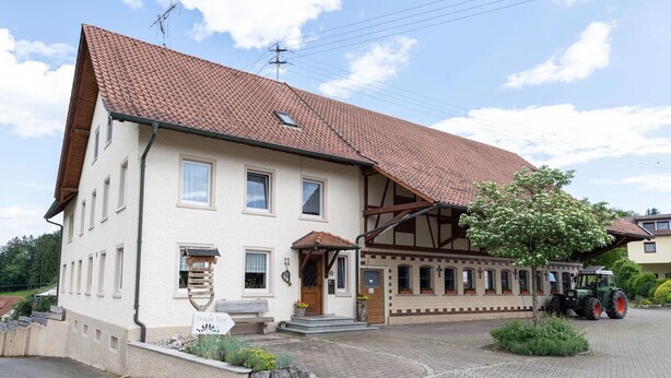 Ein zweistöckiges Haus mit einem Ziegeldach, einer Veranda und einem abgestellten Traktor.