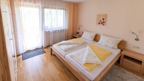 Ein Schlafzimmer mit einem hölzernen Bett, einem Nachttisch, einer Wandleuchte und einem Fenster mit transparenten Vorhängen.