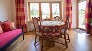 Ein Zimmer mit einem Holzesstisch, Stühlen, einer Couch und großen Fenstern mit Vorhängen.