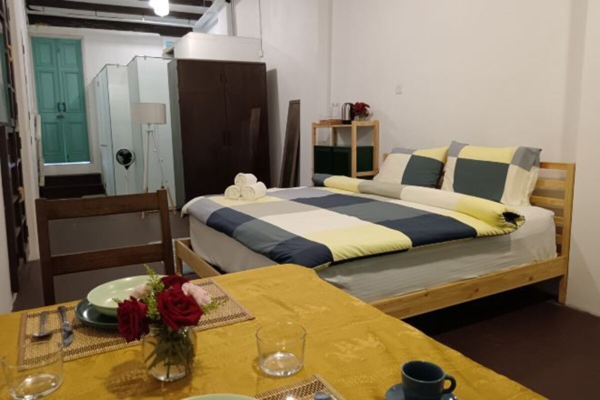 Une chambre à coucher avec un lit, une chaise en bois, une table ornée d’un vase de fleurs et une petite table de chevet avec une lampe.