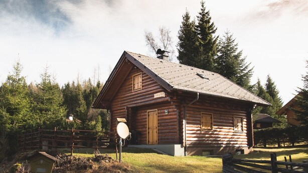 Une cabane en rondins avec un toit à deux versants, des volets en bois et une cheminée.