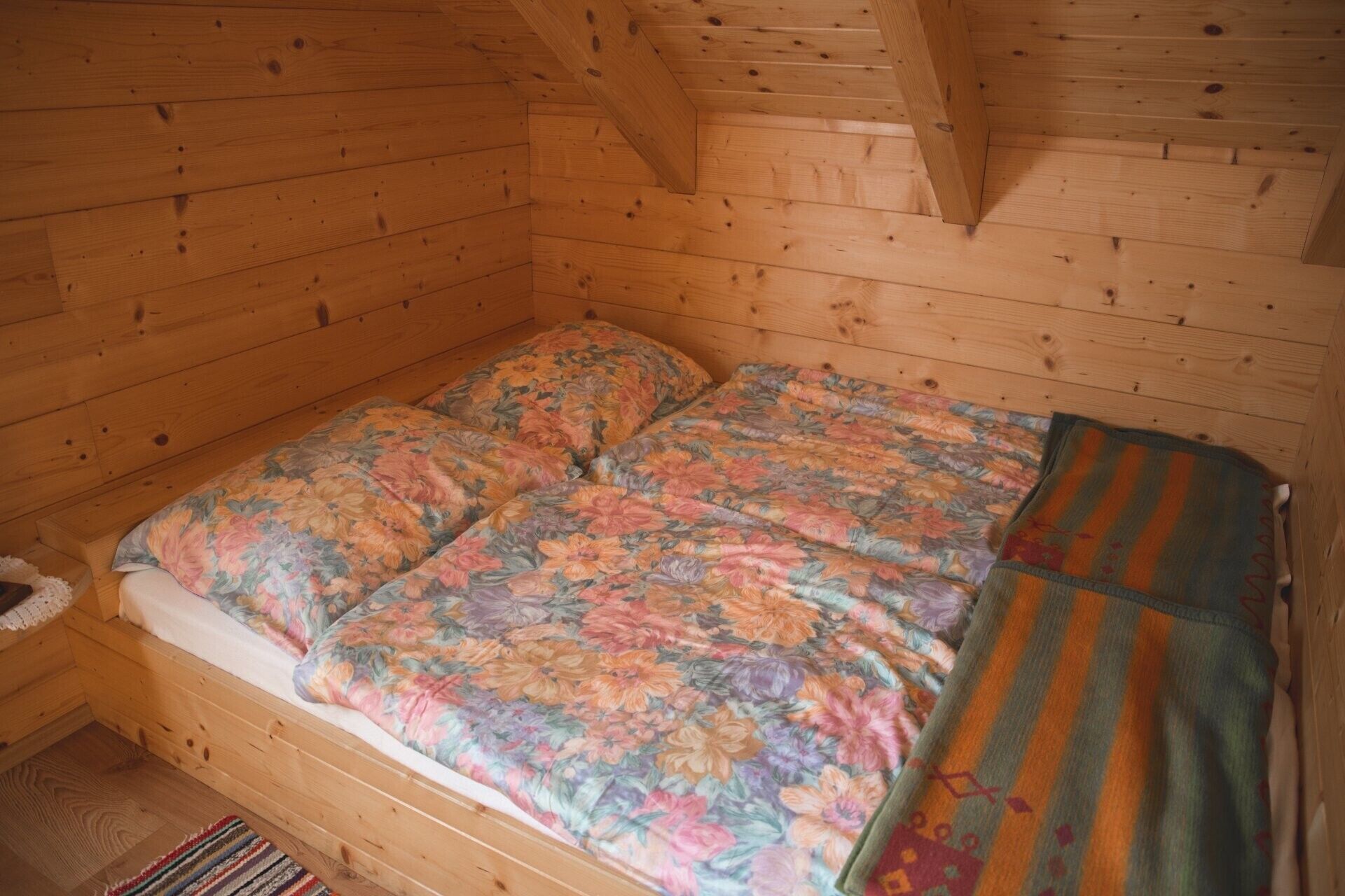 A wooden cabin interior with a bed, a small table, and a window.