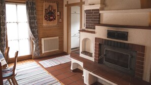 Une pièce chaleureuse avec une cheminée, des poutres apparentes, un radiateur et un tapis à motifs.