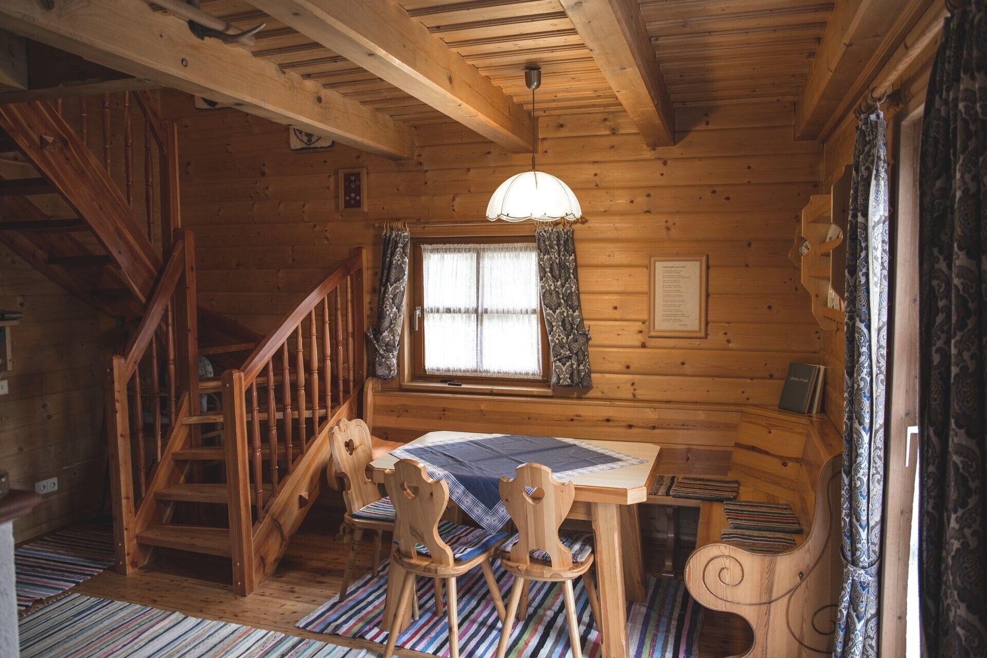 L’intérieur d’un chalet en bois comprend une table à manger, des chaises, un escalier et une fenêtre avec des rideaux.
