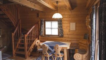 L’intérieur d’un chalet en bois comprend une table à manger, des chaises, un escalier et une fenêtre avec des rideaux.