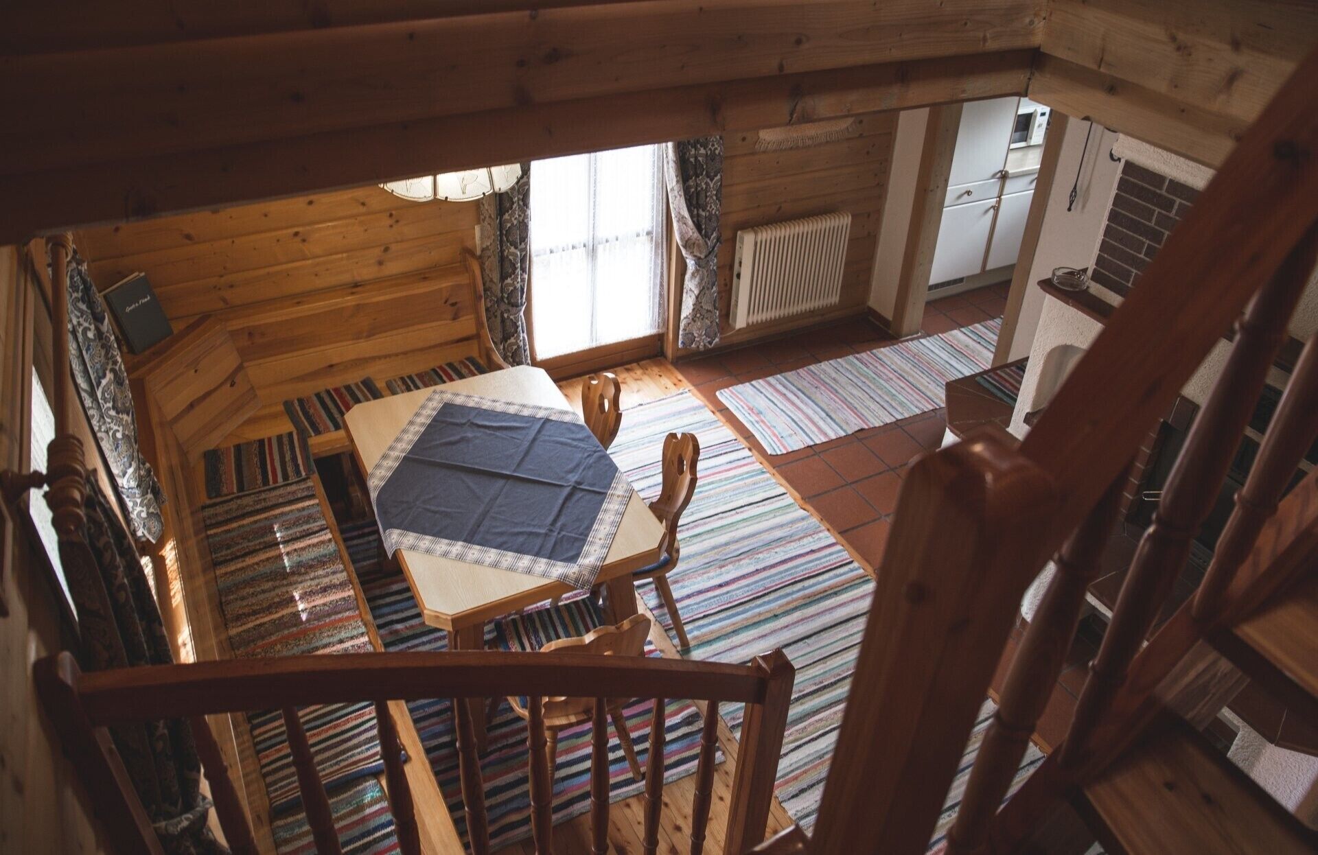 A wooden cabin interior with a loft bedroom, a dining area, and a kitchen.