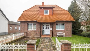 A two-story brick house with a tiled roof, a front porch, and a white picket fence. - Apartment “Cosy in Soltau” with Private Terrace, Wi-Fi, and Air Conditioning (Soltau)