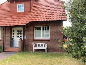 A brick house with a red-tiled roof, a white front door, a bench, and a small window. - Apartment “Cosy in Soltau” with Private Terrace, Wi-Fi, and Air Conditioning (Soltau)