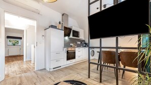 A modern kitchen with white cabinets, a microwave, oven, and a dining area with brown chairs. - Apartment “Cosy in Soltau” with Private Terrace, Wi-Fi, and Air Conditioning (Soltau)