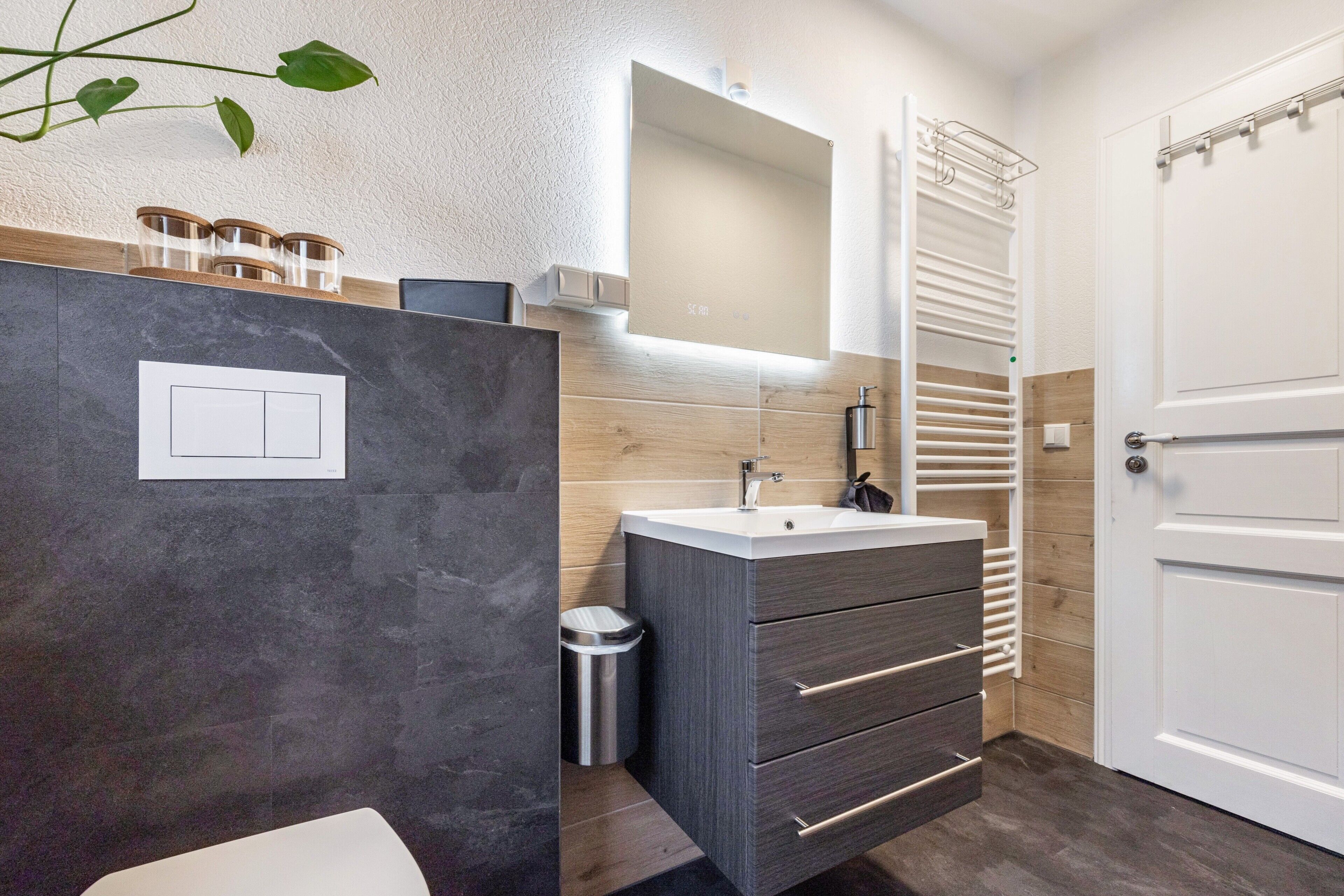 Un baño con un lavamanos moderno, un espejo, un perchero para toallas y una puerta.