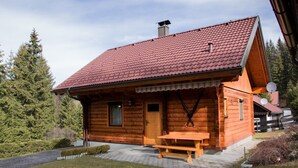 Una cabaña de troncos con techo de tejas rojas, una puerta de madera y un banco en el exterior.