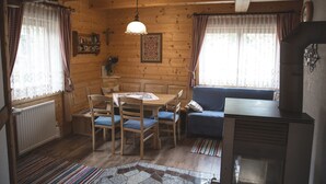 Interior acogedor de una cabaña con una mesa de comedor, sillas, un sofá azul, una lámpara colgante y un radiador.