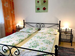 Un lit avec une literie à motifs floraux, une tête de lit en métal, deux lampes de chevet et un mur orné d’un tableau représentant des fleurs.