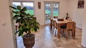 Uma sala de jantar com uma mesa e cadeiras de madeira, um vaso com planta e vista para o exterior através de portas de vidro.