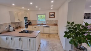Cozinha moderna com armários brancos, uma ilha central, forno embutido e janela que oferece luz natural.