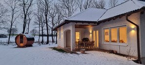 A cozy cabin with a wooden exterior, a dining area with chairs, and a large barrel in the snow. - Holiday Home 'Q1' with Private Terrace, Private Garden and Wi-Fi (Zülpich)