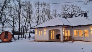 Uma casa coberta de neve com um barril de madeira, uma área de refeições e uma janela grande.