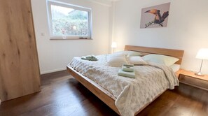 Une chambre à coucher avec un lit en bois, une fenêtre donnant sur un beau paysage, une œuvre d’art accrochée au mur et des lampes de chevet.
