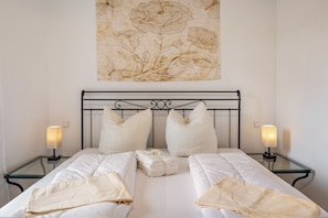 Ein Doppelbett mit weißen Leinen, zwei Nachttische mit Lampen und ein Blumenbild an der Wand.
