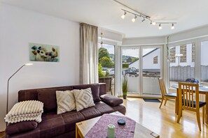 Un salon avec un canapé marron, une table basse, une table à manger avec des chaises, une grande fenêtre et un tableau accroché au mur.