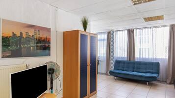Een kamer met een televisie, een houten kledingkast, een blauwe bank en een stadsgezicht schilderij.