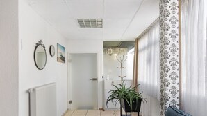 Un couloir avec un radiateur, un miroir, un tableau encadré, une plante en pot et un canapé bleu.