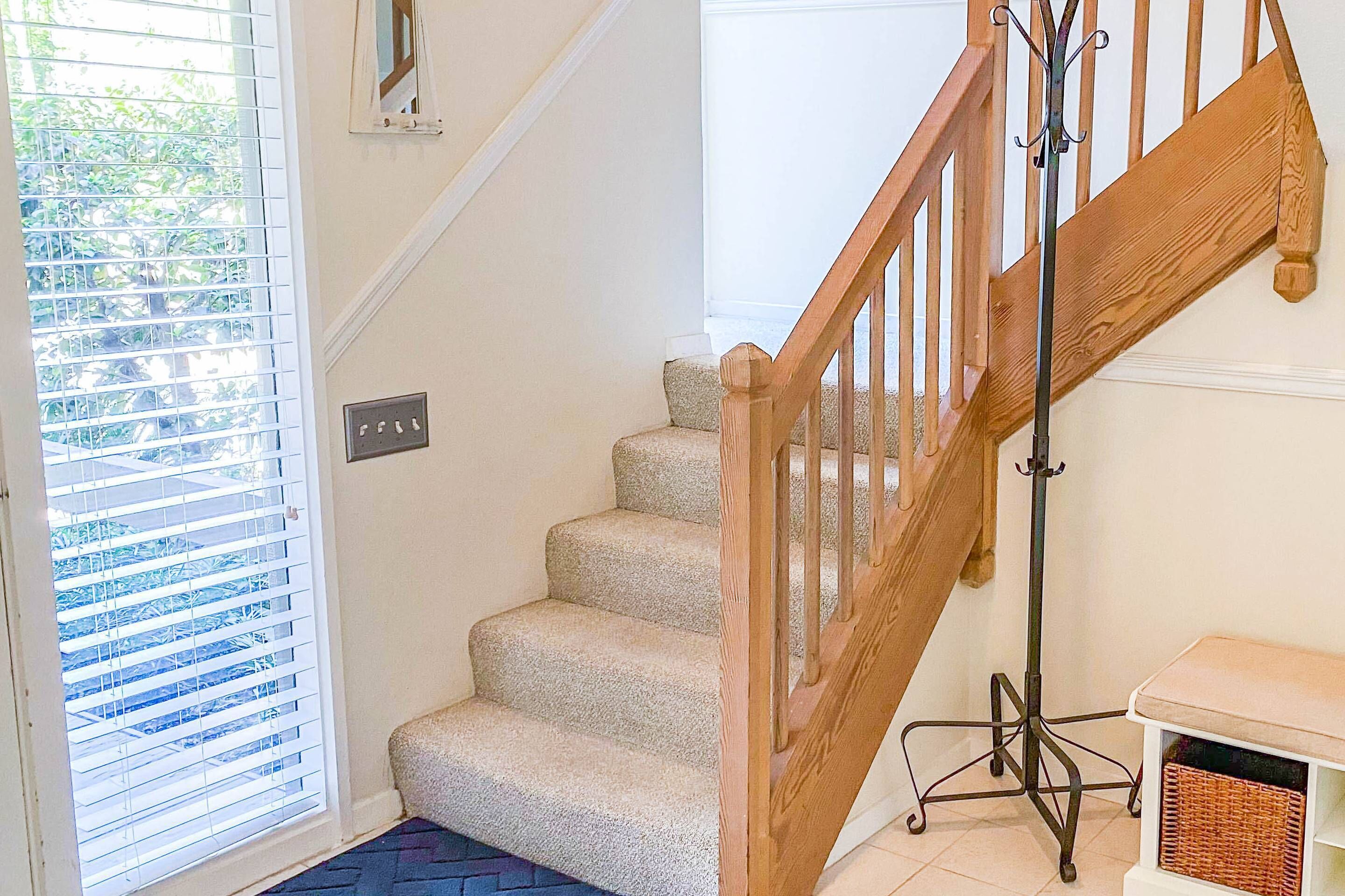 Un escalier avec des rampes en bois et des marches recouvertes de moquette, menant à l’étage supérieur.
