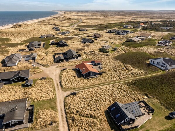 Vista aérea de una zona residencial costera con casas, dunas de arena y una playa.