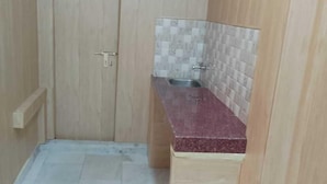 A small, enclosed bathroom with a wooden door, a tiled backsplash, and a marble countertop. - Banaras Home Stay By GRB (Varanasi)