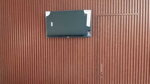 A room with a slatted wooden wall, a black object on the wall, and a small door. - Banaras Home Stay By GRB (Varanasi)