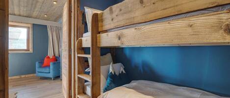 A bunk bed with a wooden frame, a blue wall, and a window with curtains.