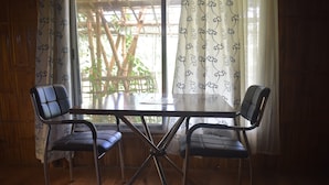 A dining table with four chairs, a window with bamboo lattice, and curtains with a pattern. - Villagelife (Mikirbheta)