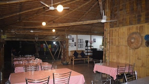 A rustic restaurant with bamboo walls, checkered tablecloths, and ceiling fans. - Villagelife (Mikirbheta)