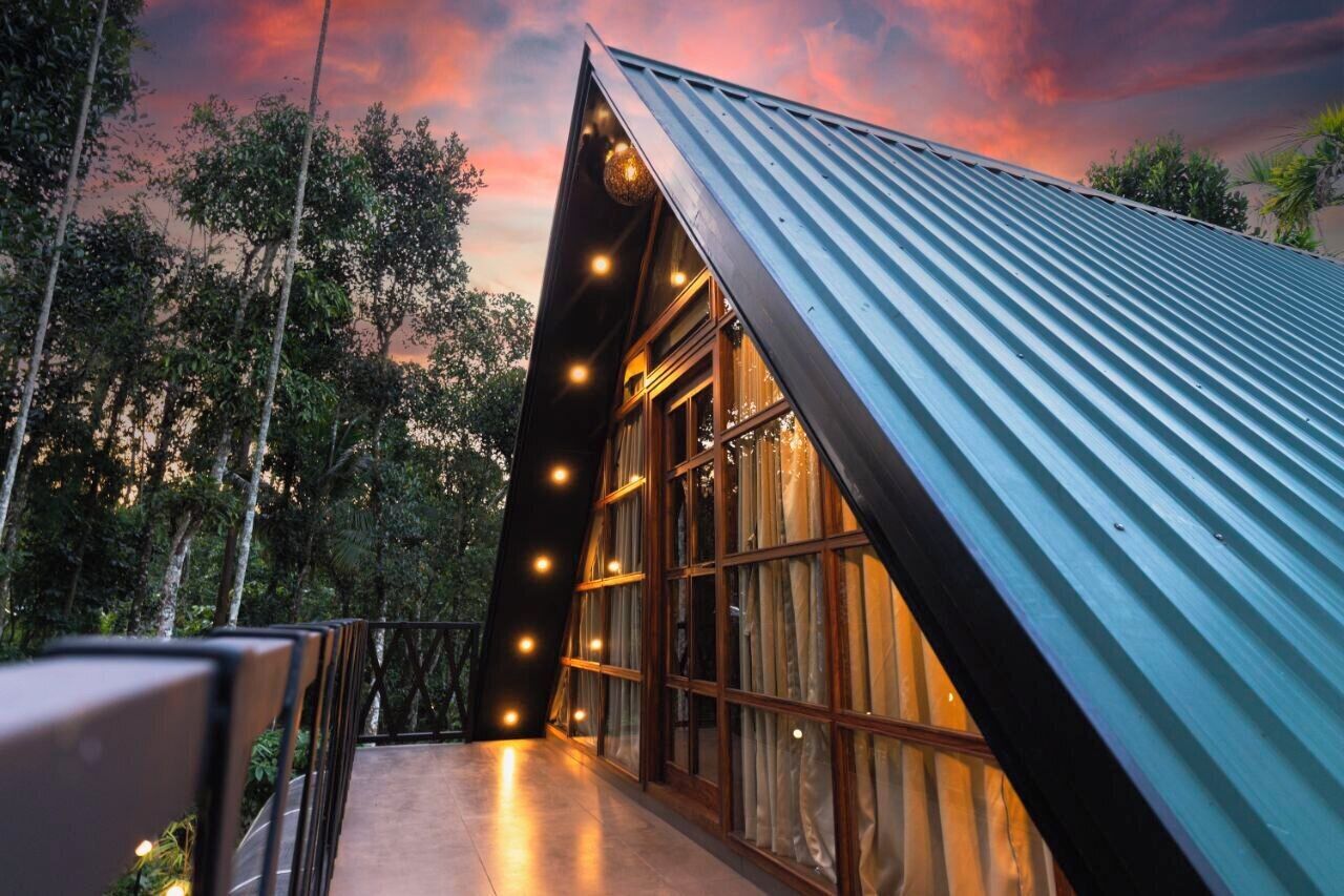 A modern building with a sloped roof and large windows, surrounded by trees.