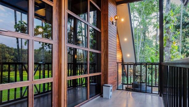 A spacious balcony with large windows offering a view of a lush garden. - Ethnic Villa Wayanad (Sulthan Bathery)