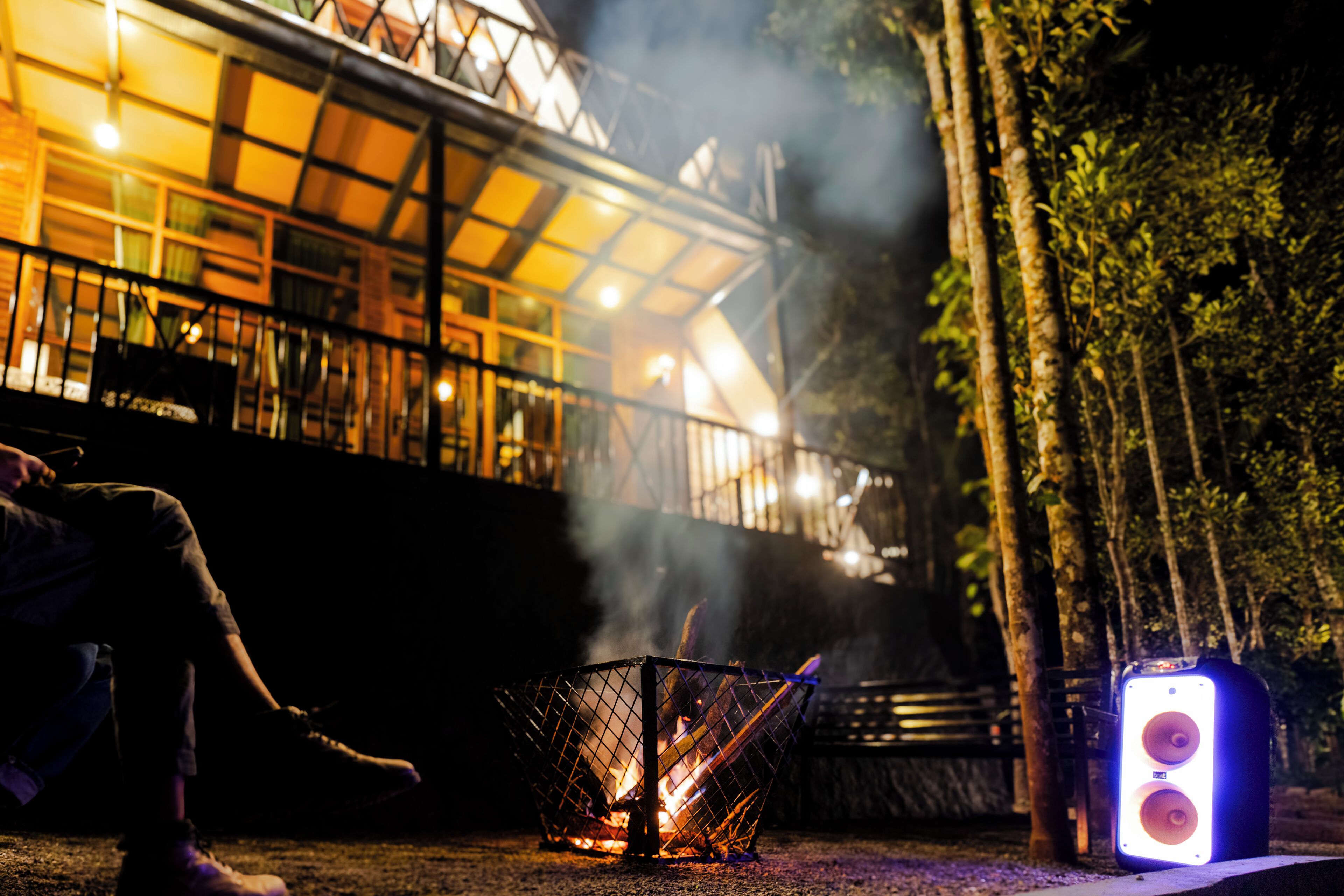 Ein Lagerfeuer mit Metallgrill, Lautsprecher und einer in der Nähe sitzenden Person.