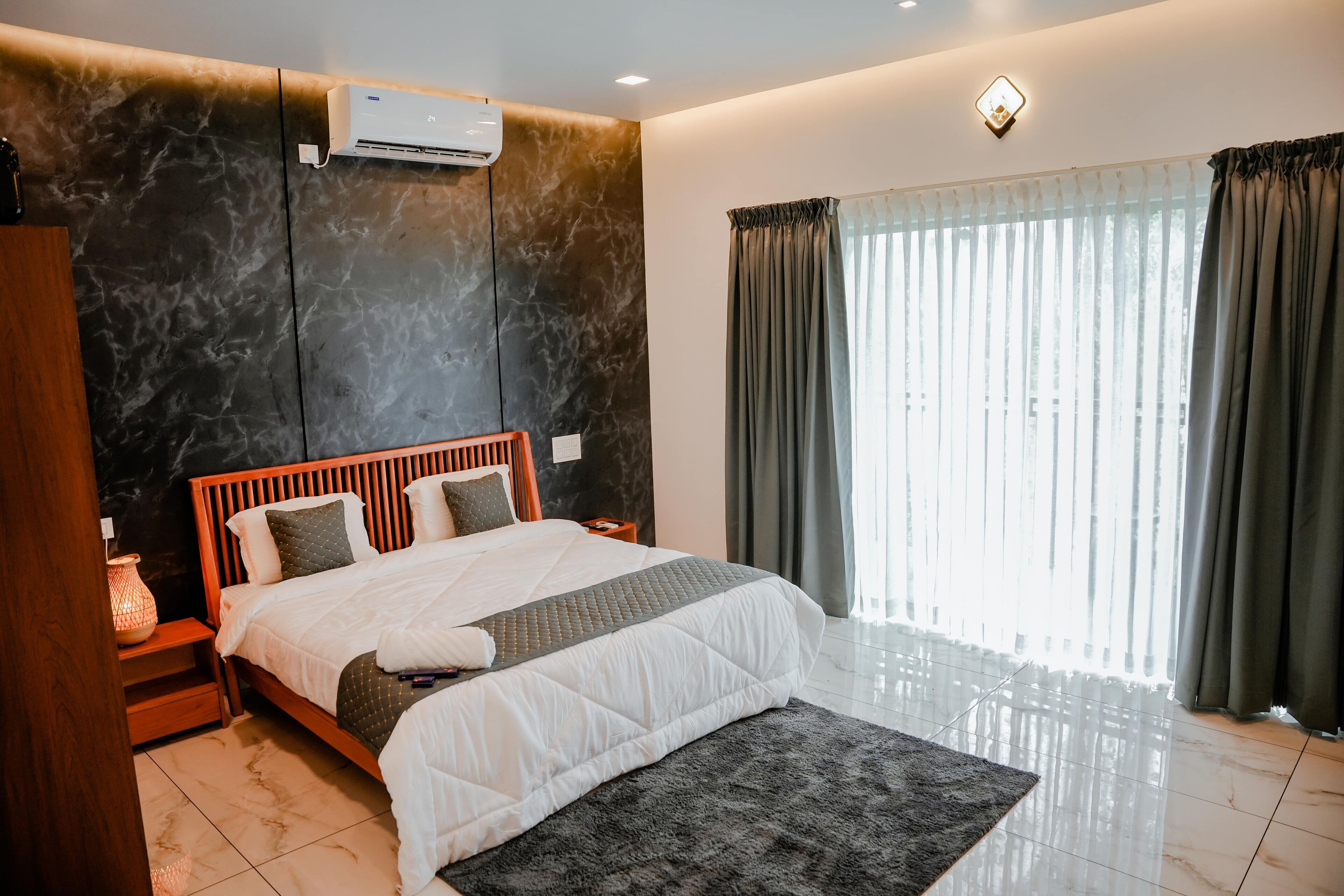 A modern bedroom with a large bed, a nightstand, a wall-mounted air conditioner, and a window with curtains.