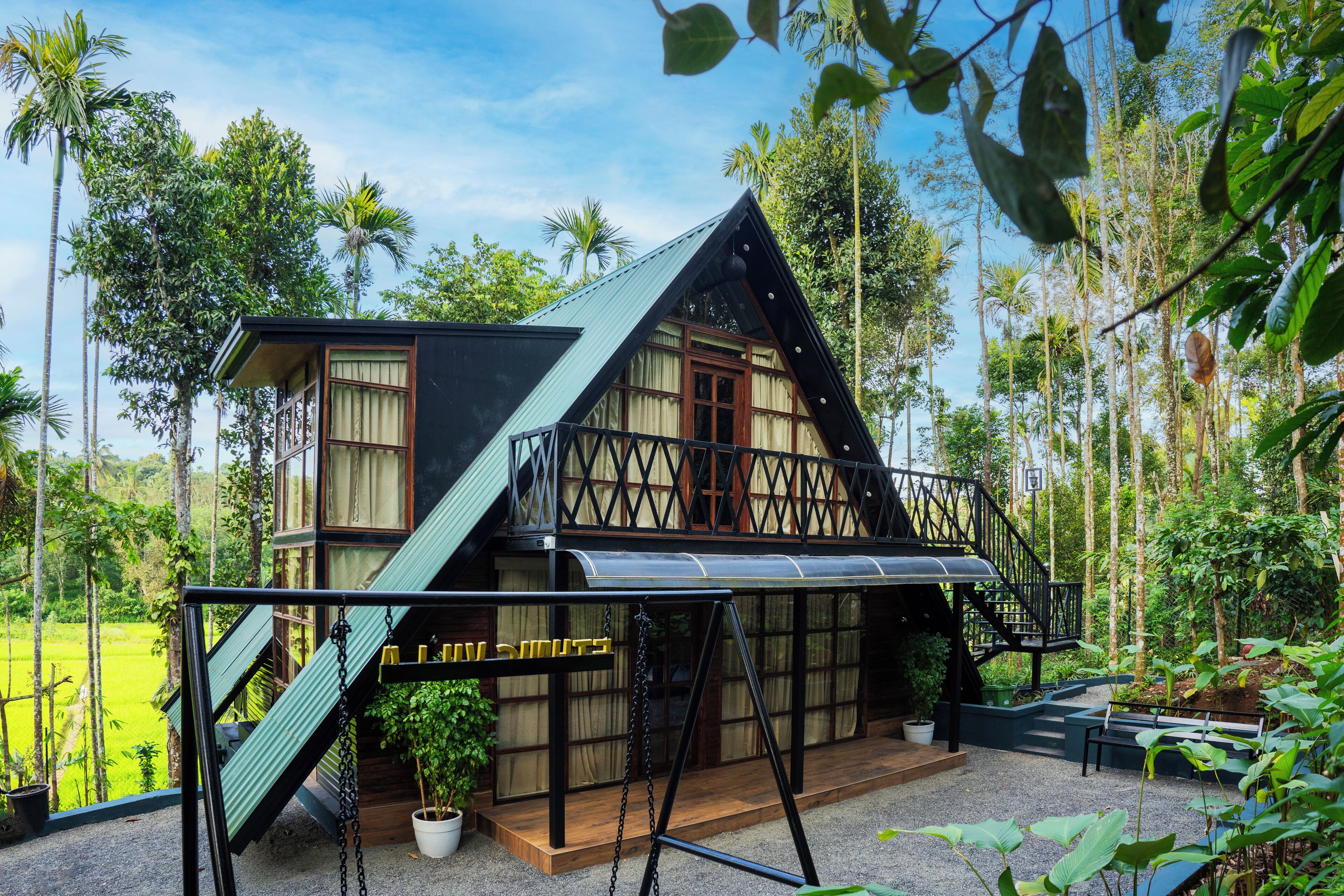 Una casa a due piani con un balcone, immersa nel verde e circondata da palme.