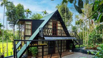 Una casa a due piani con un balcone, immersa nel verde e circondata da palme.