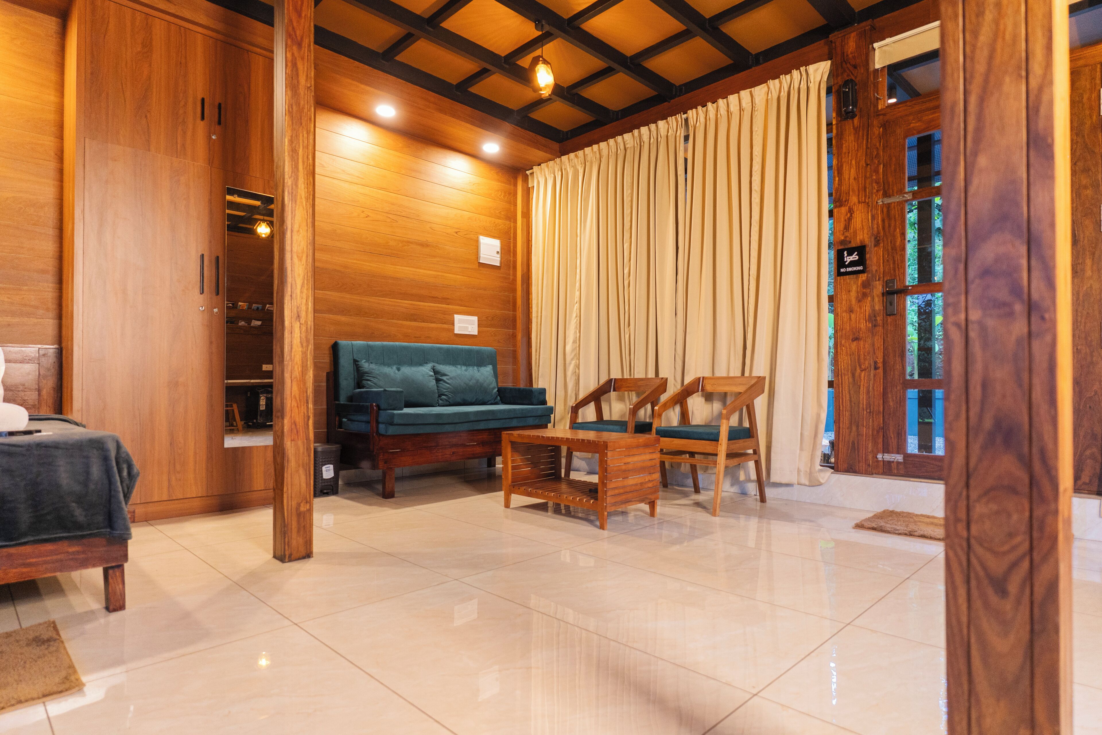 A room with a bed, a sofa, and two chairs. There is a wooden wardrobe and a door with a window.