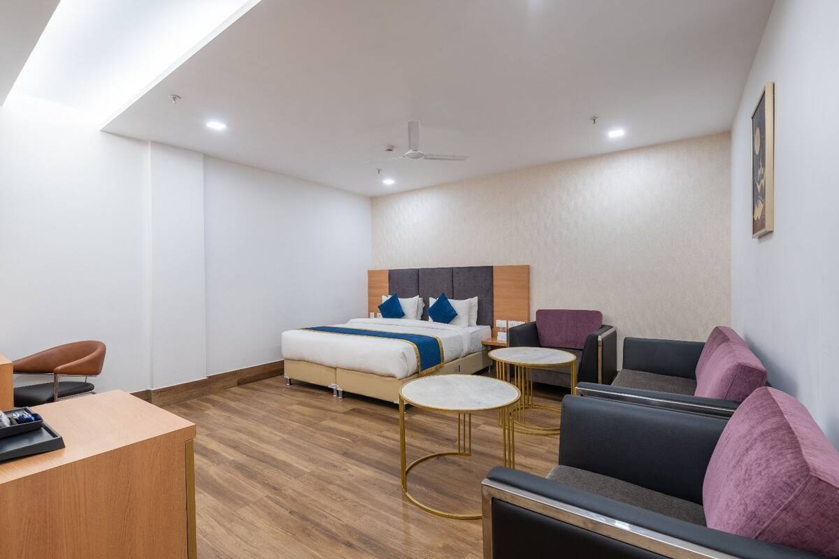 A modern hotel room with a bed, two seating areas, a desk, and a ceiling fan.