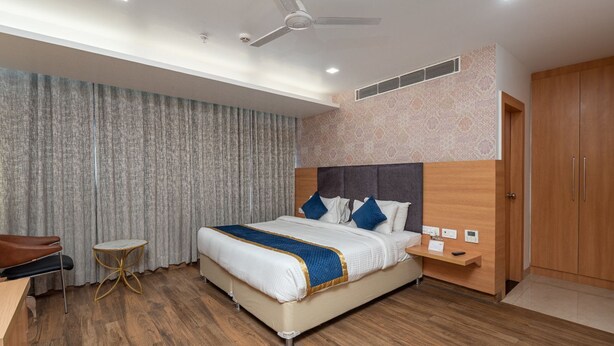 A hotel room with a large bed, a desk, a chair, a small round table, and a wardrobe. - The sandalwood by Manvenco Hospitality (New Delhi)
